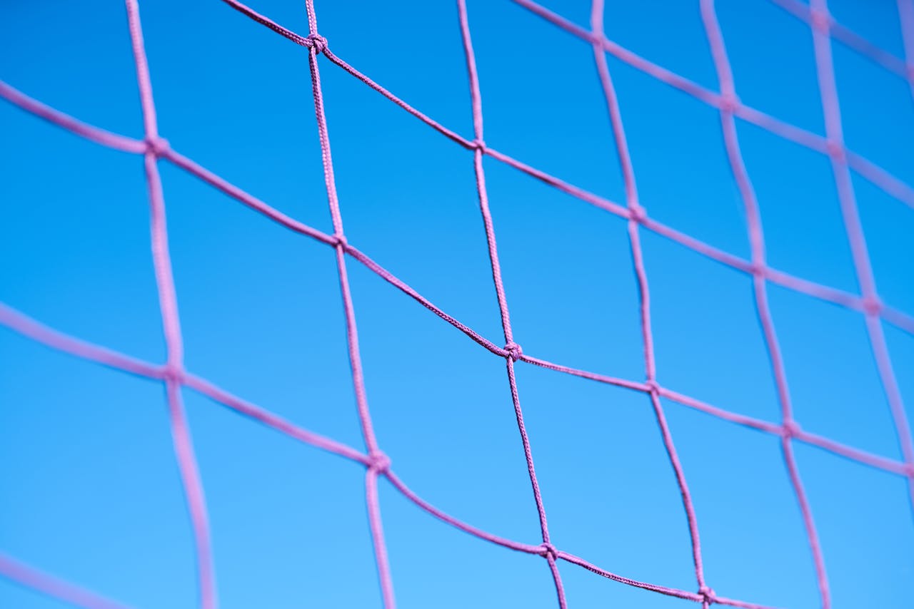 Close-up of a pink volleyball net pattern against a clear blue sky, showcasing geometric shapes.