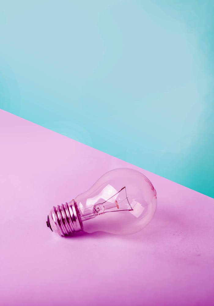 A clear lightbulb on a pastel pink and blue background, showcasing contrast and simplicity.