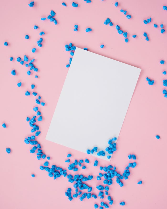 Flat lay of a white paper on a pink surface with scattered blue pebbles.